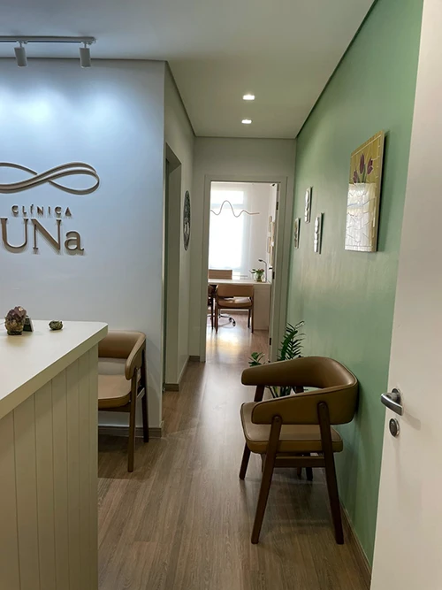 Corredor da Clínica Una, com o logotipo na parede e poltrona de espera