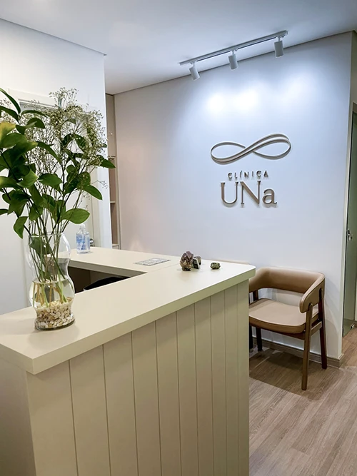 Recepção da Clínica Una, com balcão claro e o logotipo na parede